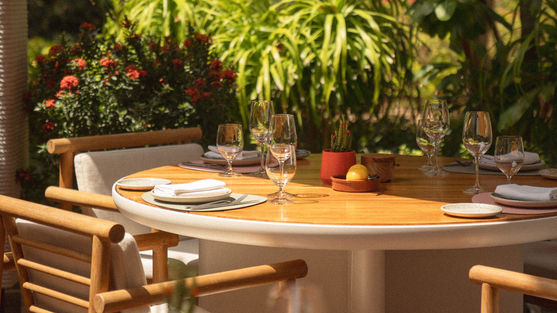 Round table set with elegant dishware and glasses, lush greenery around, at Banyan Tree Dubai Alizee pool & beach.